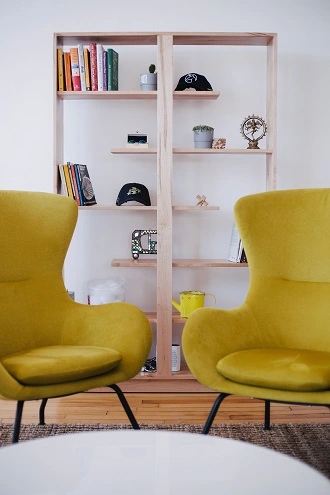 two large yellow chairs sitting on a rug in front of a bookcase filled with decorative items