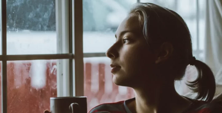 millennial woman holding coffee mug looking out window