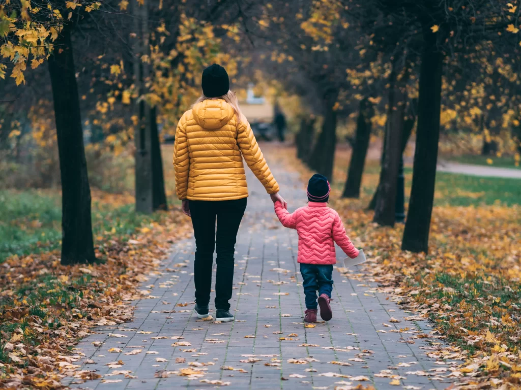 woman and child walking on path in autumn with leaves on path and ground