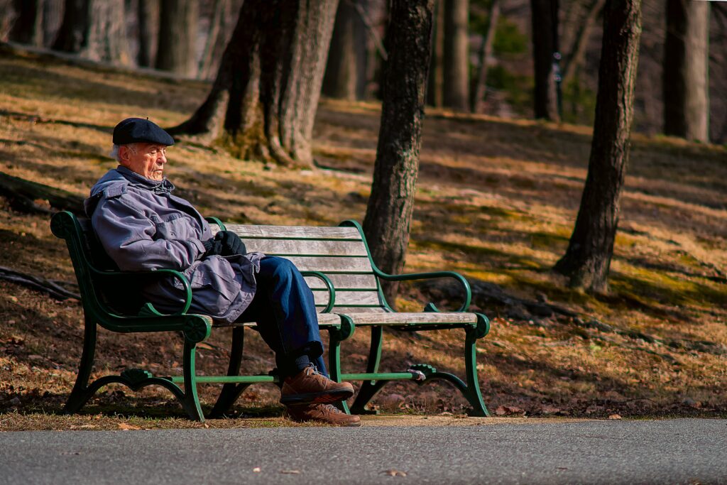 senior citizen man sitting on a park bench with trees behind him
