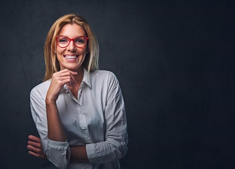 businesswoman in red glasses smiling in front of a dark background