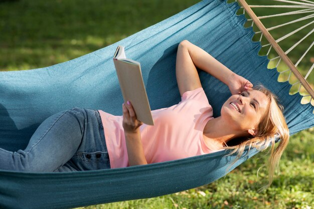 millennial woman laying on hammock reading a book in the sunshine